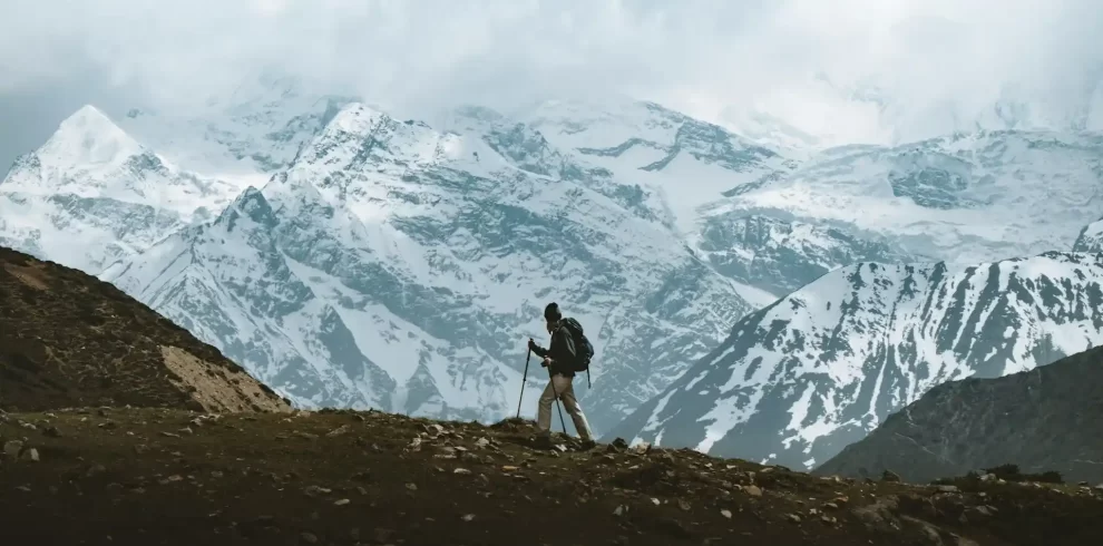 An American tourist walking on rugged terrain, gazing at the snow-capped Himalayas partially covered by clouds in Nepal