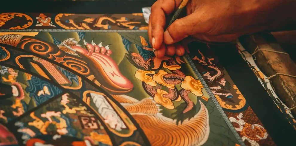 An artist carefully creating a colorful Thangka painting, filled with intricate details and traditional motifs.