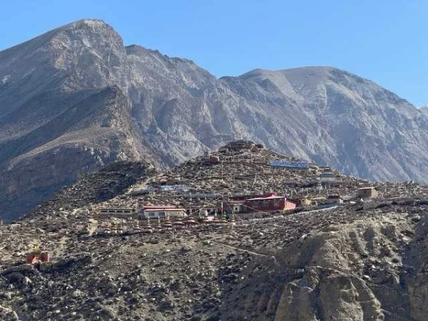 Barren landscape view of Tashi Lhakhang Monastery with a towering hill in the background, seen from Phu Village