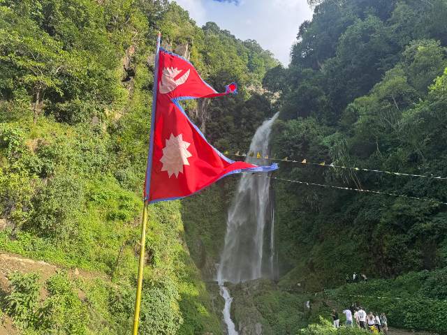 Waterfall in Ngadi Village, Lamjung, Nepal, adorned with a fluttering Nepal flag.