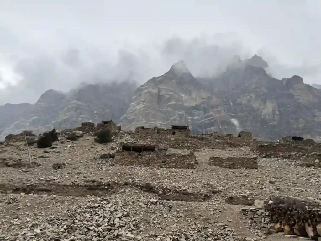 Chyakhu Village in Nar Phu Valley, a remote stone settlement against a backdrop of jagged, cloud-shrouded Himalayan peaks.