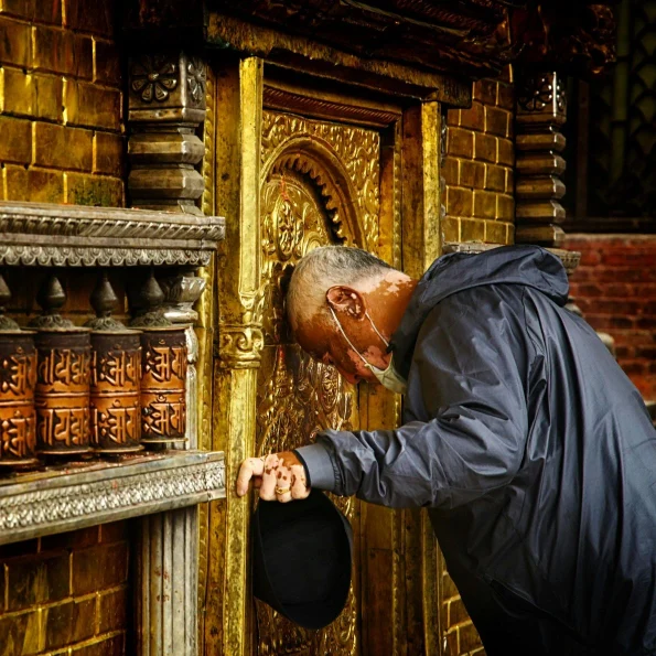 A Newari Man, from Nepal, bowing his head in the Buddhist Temple golden door